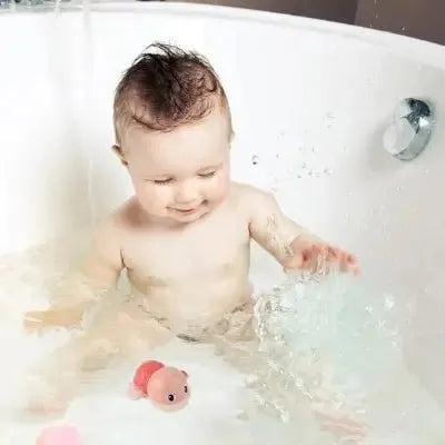 Bébé riant avec jouet aquatique rose dans baignoire blanche